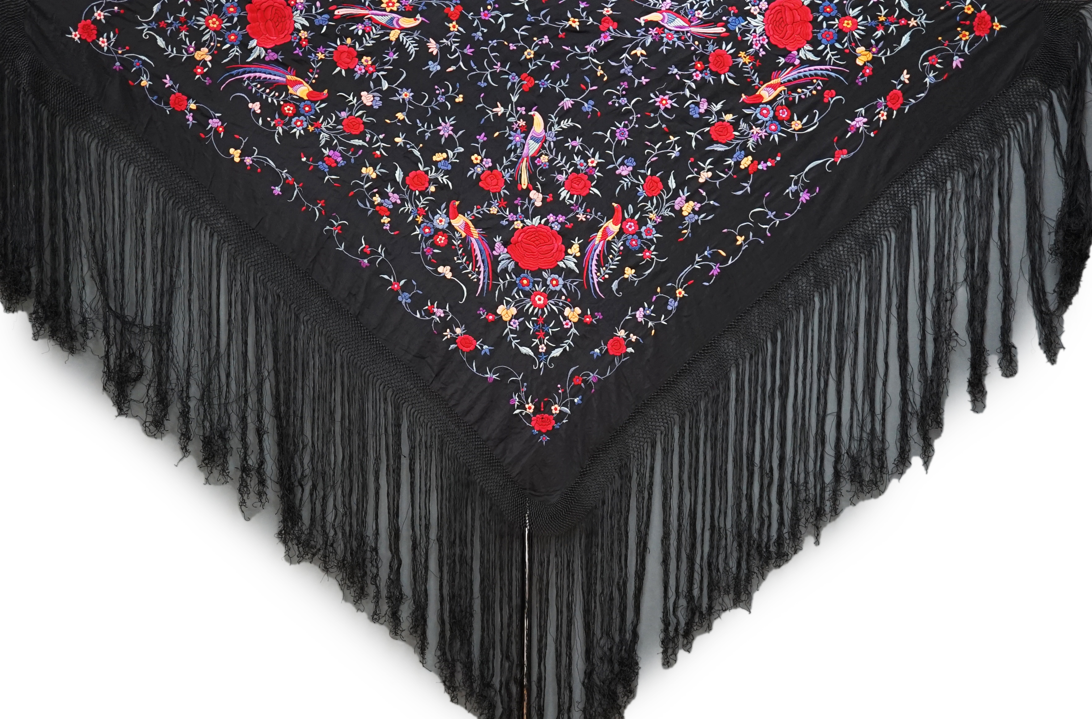 An early 20th century Chinese black silk fringed shawl with polychrome silk embroidery, embroidered with meandering floral design, the corners embroidered with three brightly coloured birds of paradise, large red roses a